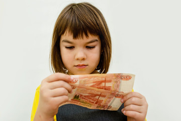 a girl of 8 years of Asian appearance holds in her hands banknotes of 5 thousand Russian rubles on...