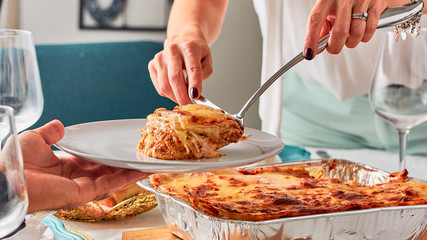 woman serving portion of lasagna food on a family table. Traditional Italian food - obrazy, fototapety, plakaty