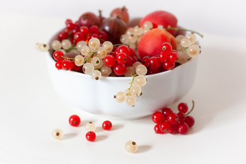 A white bowl full of red and white currants and apricots.