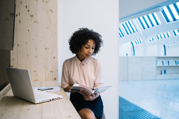 Successful young black female employee looking through catalog in business hall