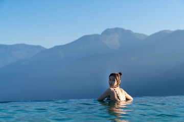 Sexy woman relaxing in infinity swimming pool   with stunning mountain view at  luxurious resort / vacation concept