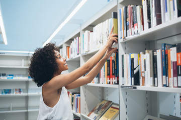 Happy African American woman taking book from bookshelf