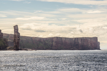 ocean view of Old Man of Hoy, a tall sandstone stack at the coast between Stromness and Scrabster at Orknay in Scotland, Uk. Famous British climbing place at cliffs with stunning clouds in the sky