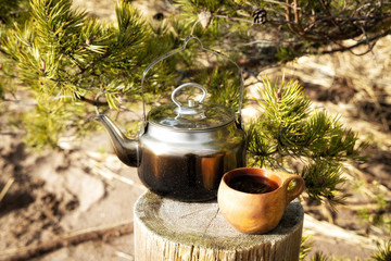 Hot drink in the morning outdoors. Camp kettle and mug standing on tree stump in the mountains.  - Powered by Adobe