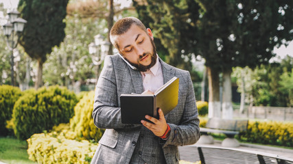 Fototapeta premium Businessman is talking on phone and writining something in notebook