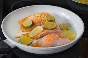 Bio Lachsfilet auf der Haut gebraten in einer weißen Pfanne mit Zitronen- und Limettenscheiben