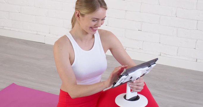 Smiling young soman sitting on yoga mat and browsing on her tablet. Online learning concept