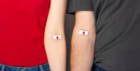 Blood donorship. Man in grey and woman in red T-shirt with hands taped patch after giving blood...