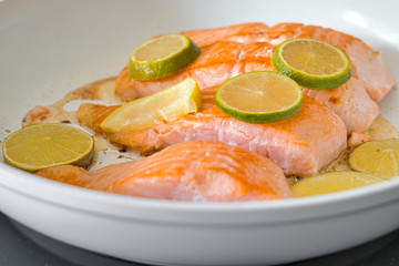 Bio Lachsfilet auf der Haut gebraten in einer weißen Pfanne mit Zitronen- und Limettenscheiben