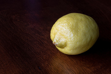 A single whole lemon on a wooden tabletop surface. 