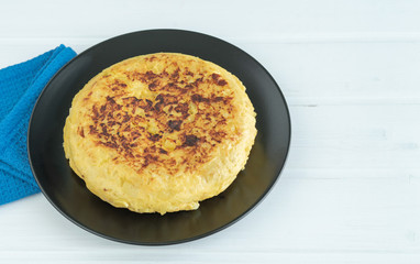 Potato omelette on a black plate on a white background. Copy space.