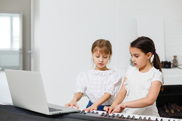 Home piano lesson. two girls practice sheet music on one musical instrument. Family concept. The idea of activities for children during quarantine.