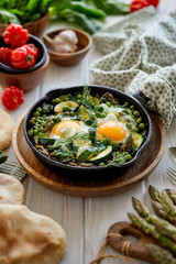 Green shakshuka with green vegetables and fried eggs in cast iron skillet on a white wooden table.