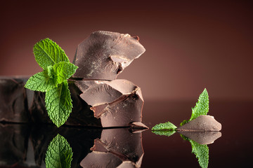 Large piece of dark bitter chocolate with mint on a black reflective background.