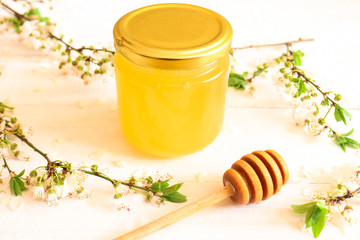 Flower honey in a glass jar on wooden background with a wooden honey dipper and blossoming branches. 