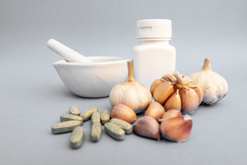 Garlic, Medicine grinding cup, Garlic tablet, White medicine bottle on gray background. Alternative medicine, herbal treatment concepts