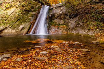 Fototapeta na wymiar Long exposure view of the beautiful Pruncea Casoca Waterfall with fallen leaves in an autumn landscape,Siriu, Buzau, Romania