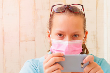Girl in medical mask at home with a phone in quarantine isolation.