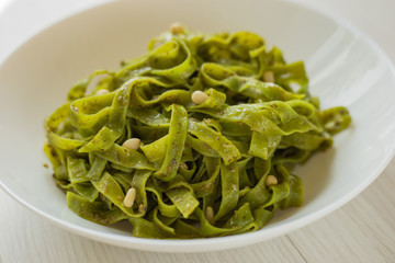 Spinach Tagliatelle . Vegan pasta with spinach, pesto sauce and pine nuts on a white plate.