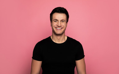 Sincere smile.  Close-up photo of a happy young man in a black t-shirt, who is looking in the camera with a cheerful facial expression.