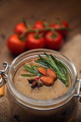 Glass jar with poultry pate, decorated with almonds and rosemary, crackers with pate and red cocktail tomatoes on the sackcloth and wooden background