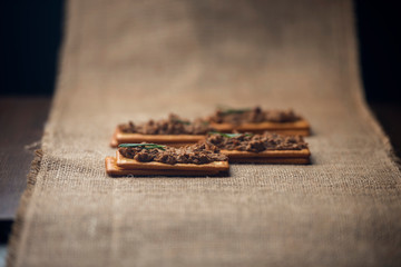 A few crackers with poultry pate on the sackcloth and wooden background,
