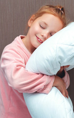 Little red-haired girl hugs a pillow and wants to sleep