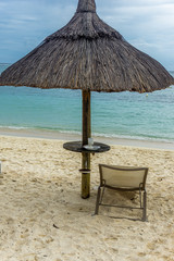 Empty chair under a thatched hut facing the ocean on a tropical sandy beach in Mauritius