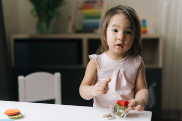 Pretty beautiful little two-year-old girl is playing with educational toy standing at the table in cozy children room.