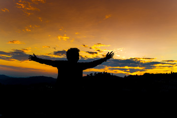 Silhouette Happy Man Standing on Hill at the Sunset on Mountain with Orange Sky. Enjoying Peaceful Moment Concept. Relaxing or achievement Concept.