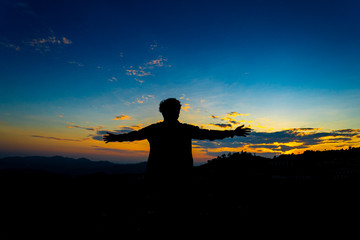 Silhouette Happy Man Standing on Hill at the Sunset on Mountain with Blue Sky. Enjoying Peaceful Moment Concept. Relaxing or achievement Concept.