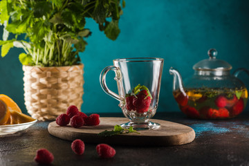 glass cup with raspberry tea mint leaves and lemon on blue