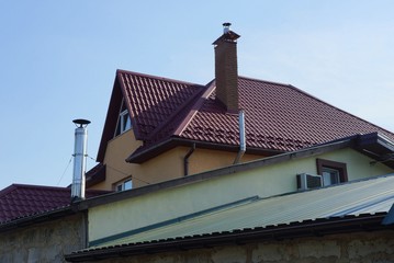 attic of a private house with a brown tiled roof and chimneys against a blue sky