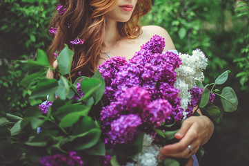 A young girl with a large bouquet of purple lilac. A girl in a Park among green trees.Beautiful spring flowers.