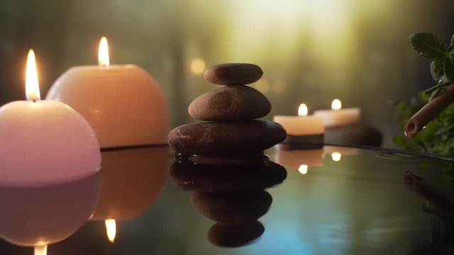 burning candles in the water, the reflection of stones on the background of evening nature, water drops falling. slow motion. Close up Concept: relaxation, wellness, body care, spa, aromatherapy