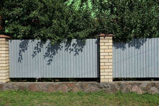 long fence wall made of gray metal and white bricks on a rural street