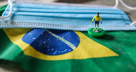 flag of Brazil with plastic football player and surgical mask for Coronavirus Prevention - Covid19 pandemic