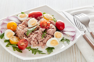 Tuna salad with arugula and tomatoes on light wooden background. Healthy food, seafood menu,