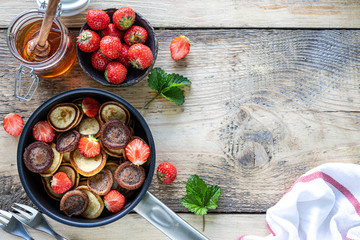 Different tiny pancake cereal in a pan with honey and strawberries on a wooden background. Top view. Copy space
