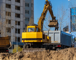 Excavator loader and dump truck during earthworks at a construction site. Loading land in the back of a heavy truck. Excavator digs land for the construction of a new park area.