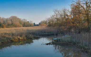 Boat in the middle of the colourful winter landscape of the Venetian lagoon of Caorle with reeds, trees and blue sea water