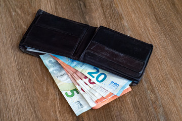 Old shabby wallet with euro money on a wooden background