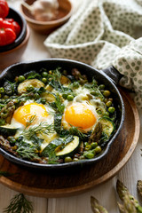 Fototapeta na wymiar Green shakshuka with green vegetables and fried eggs in cast iron skillet on a white wooden table close up view