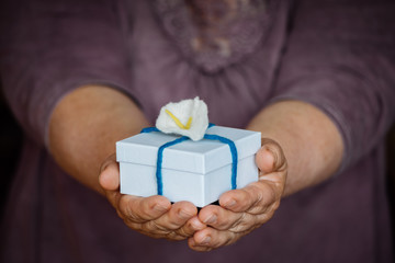 Hände halten oder überreichen eine kleine weiße Schachtel mit einer blau, türkis Schleife und einer Blume. Ein Geschenk, geringe Schärfentiefe