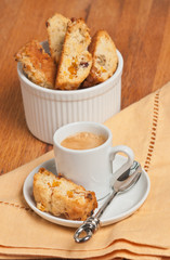 Top front view, close distance of a cup of espresso with homemade apricot, ginger walnut biscotti and ramekin filled with freshly baked biscotties