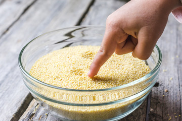 Finger touching millet seeds from glass bowl