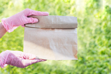 Contactless delivery. Hands in pink medical gloves hold out an order in a craft package on a background of trees
