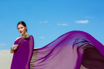 Amazing beautiful brunette woman with the Peacock feather in purple fabric in the desert. Oriental, indian, fashion, style concept