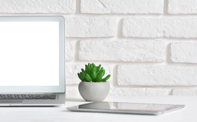 White desktop with laptop and tablet on a background of a white brick wall with a copy space