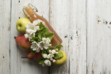 Bottle of apple and pear juice, fresh pears, apples and flowers on a white wooden background. Country style